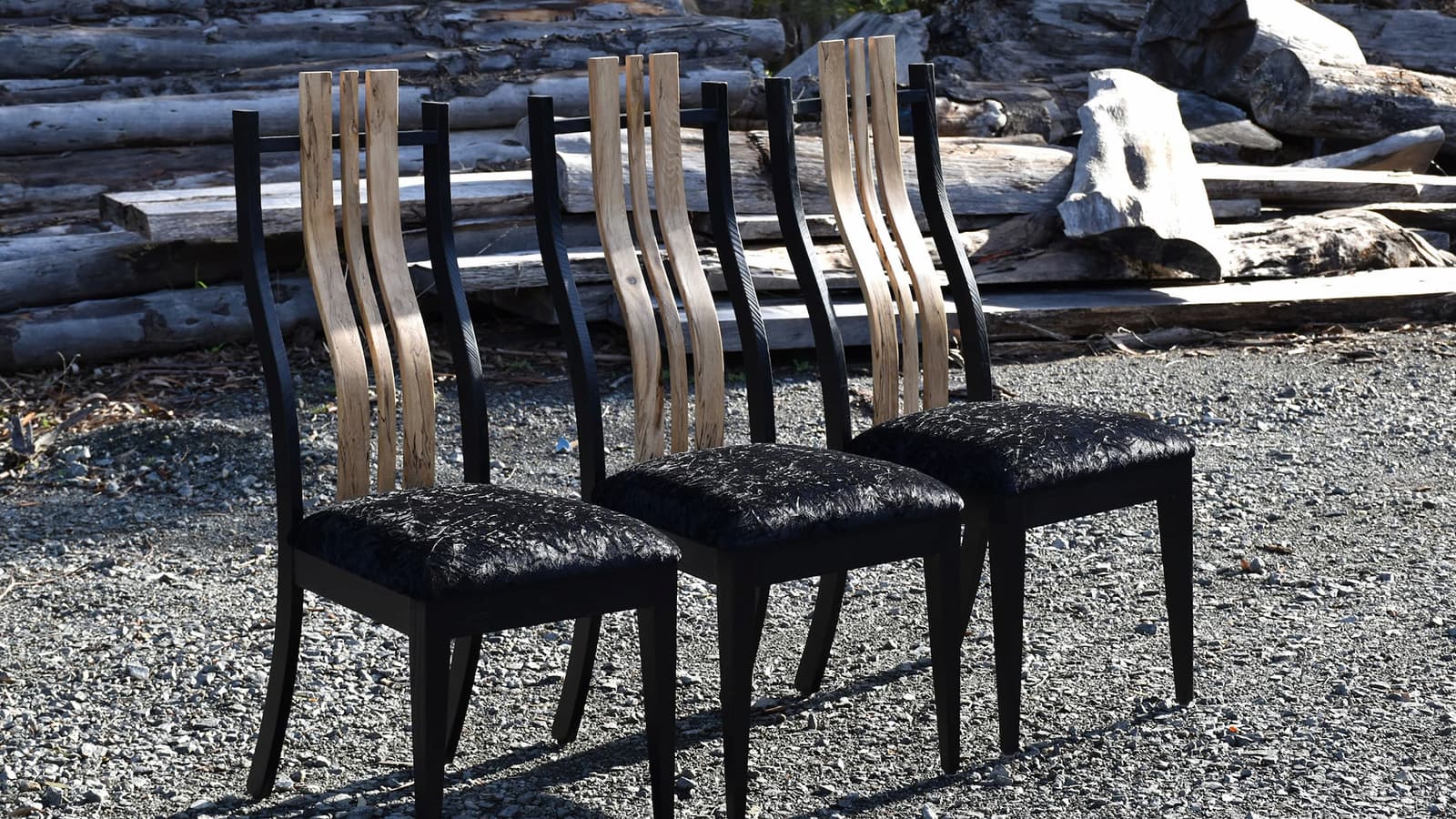 Three handcrafted timber dining chairs with black upholstery outdoors.
