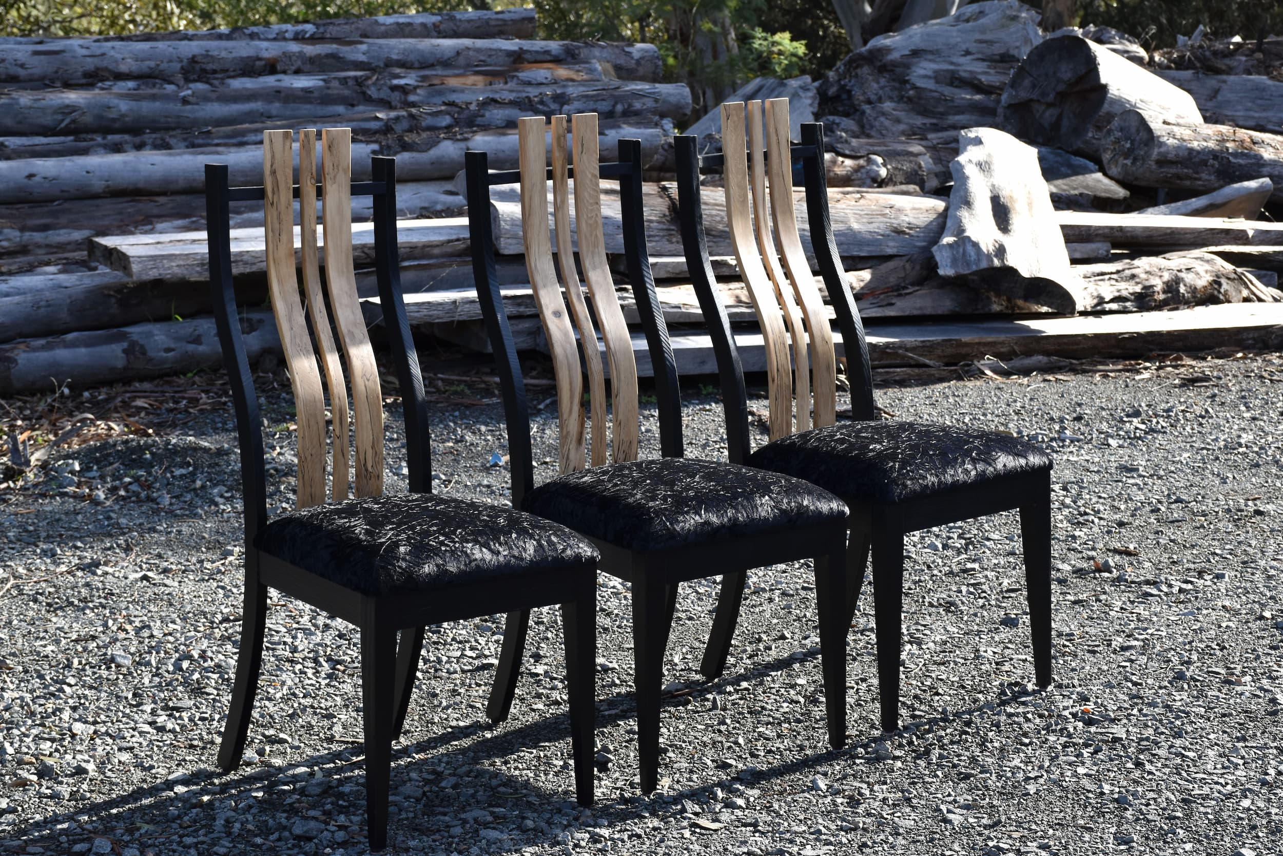 Three handcrafted timber dining chairs with black upholstery outdoors.