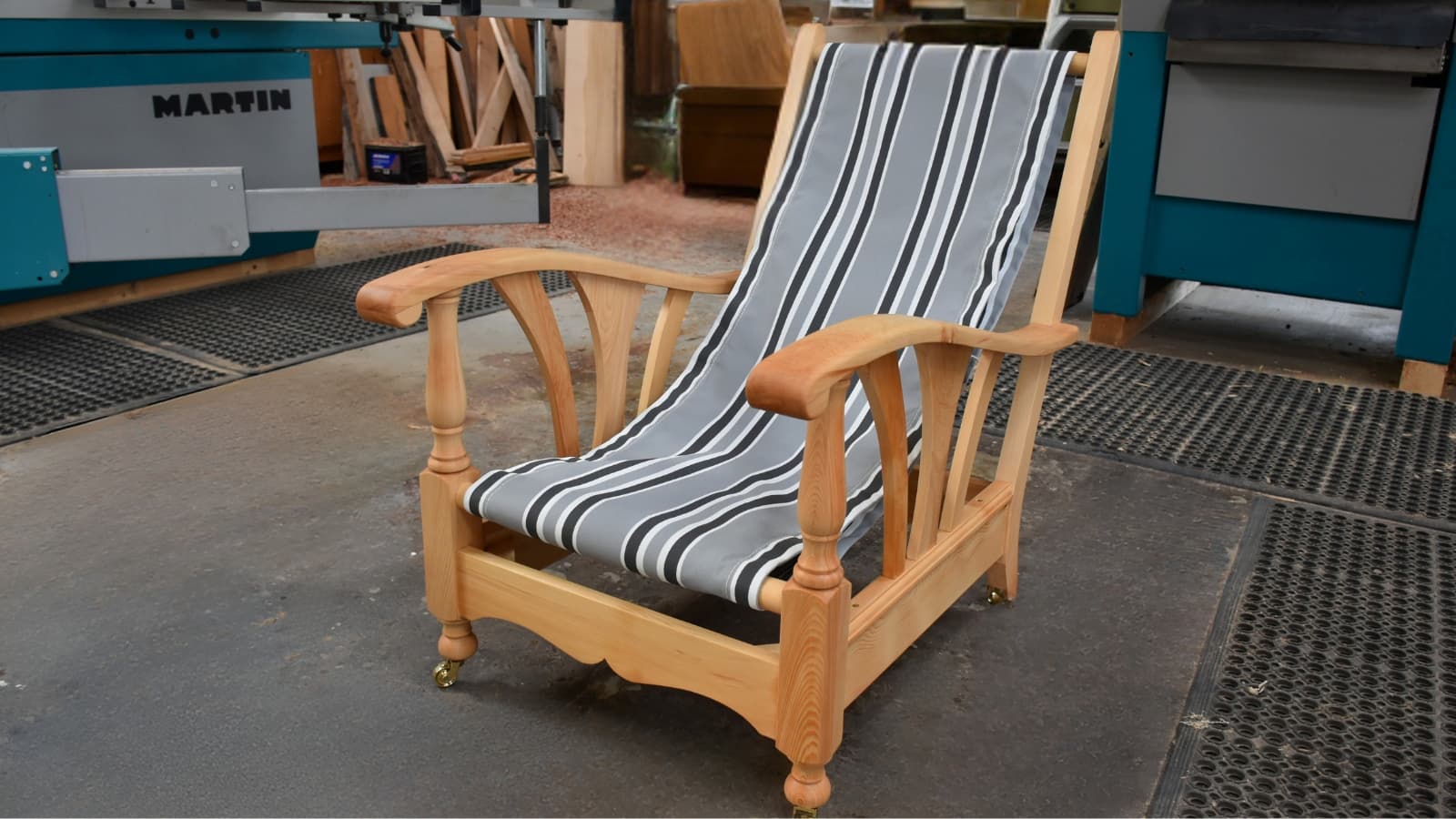 Handmade timber deck chair with striped fabric seat in workshop.