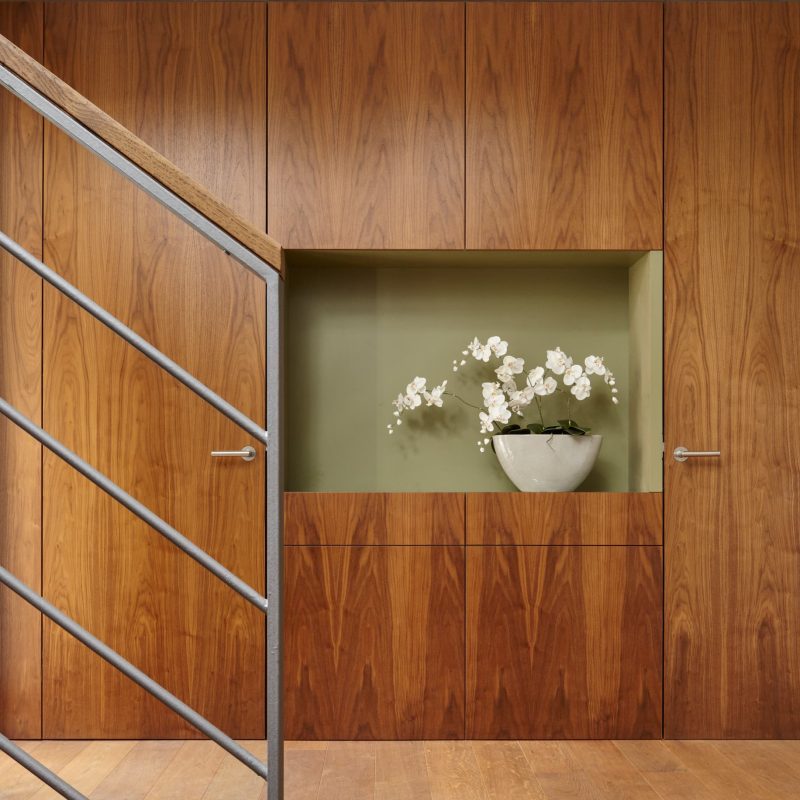 A modern interior with rich walnut wood paneling, a built-in niche featuring a green accent wall, and a white orchid arrangement.